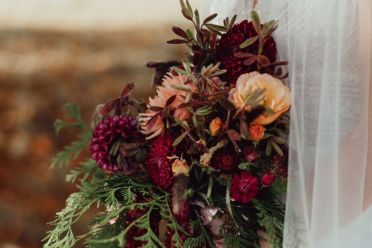 Close-up of autumn bridal bouquet with burgundy dahlias, peach roses, and rich greenery